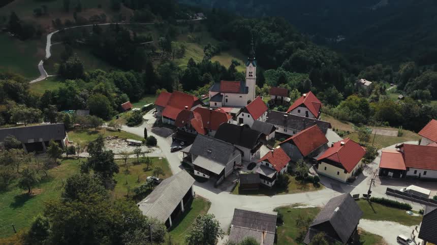 An aerial view of a small village nestled in a green landscape with a prominent church and redroofed buildings