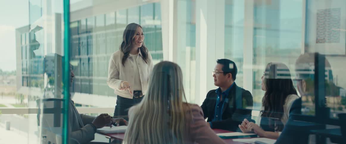 Woman standing at an office desk and interacting with other people in a cheerful manner