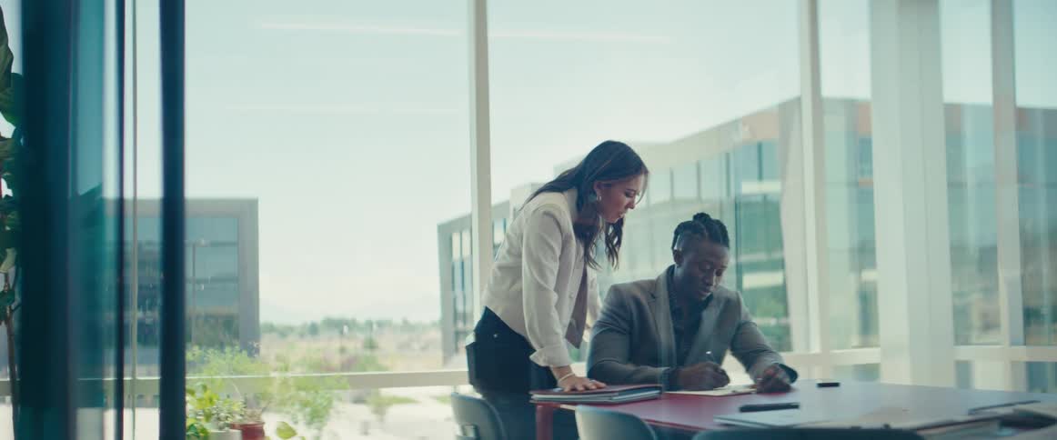 Colleagues in a modern office with large windows are engaged in a discussion over a document on the table