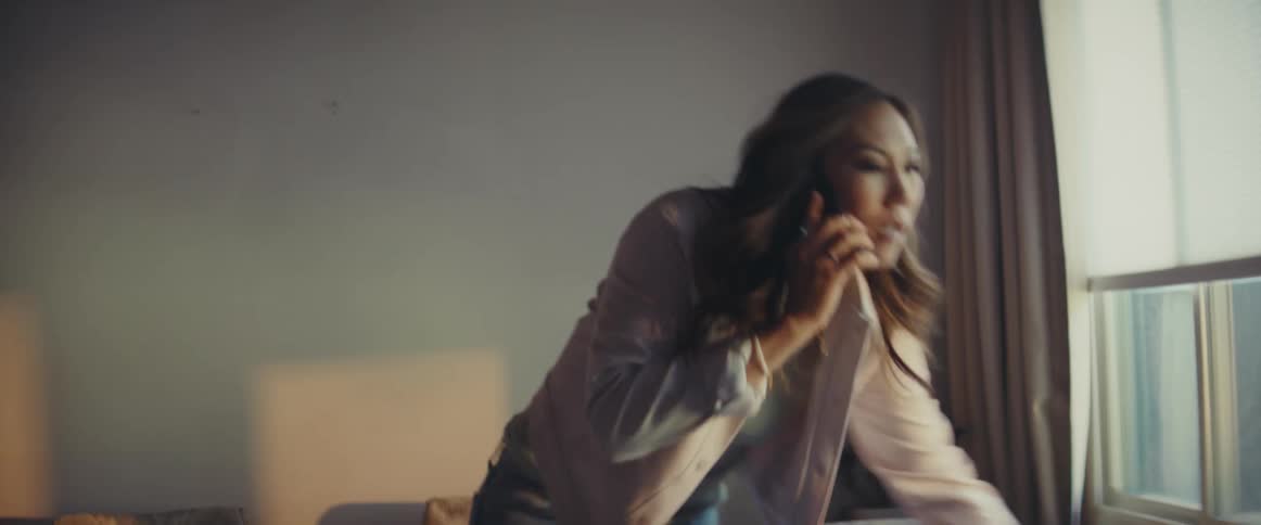 A woman talking on a smart phone as she frantically searches her living room for something