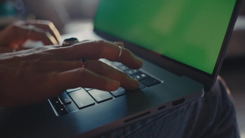 A person types on a laptop with a green screen