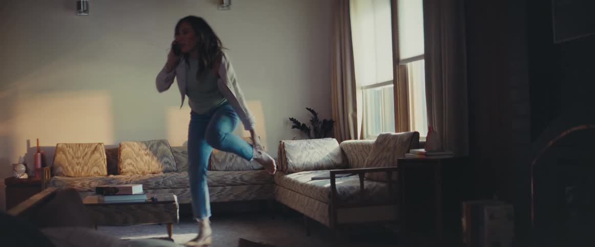 A woman dresses in the living room as she talks on her cell phone