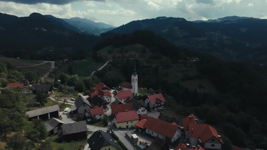 A recreational vehicle drives through a small village located near mountains