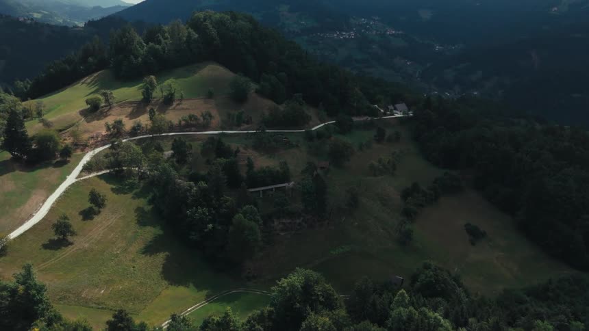 Aerial view of a steep green mountain with scattered trees and trails