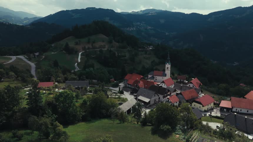 An aerial view of a small village nestled in a lush green valley with rolling hills and mountains