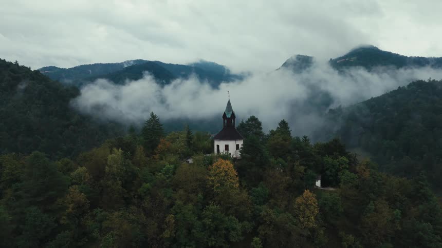 Aerial of a steeple building on a mountain top in a remote forest