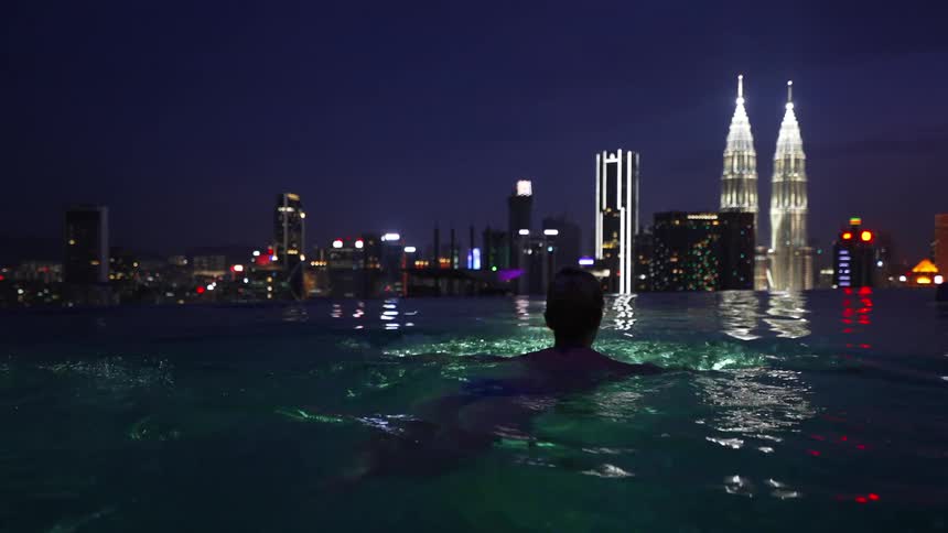 Woman swimming in a pool overlooking a metropolis with illuminated skyscrapers at night