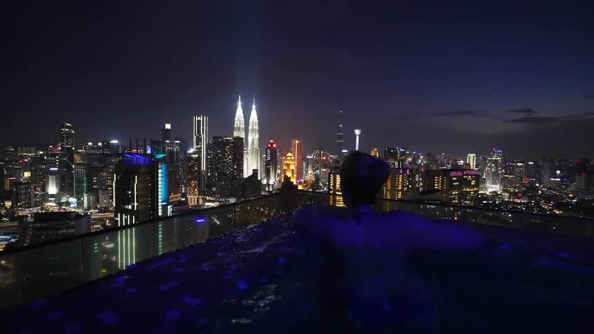 A woman swimming in a balcony pool on a skyscraper approaches the edge to take in the city skyline