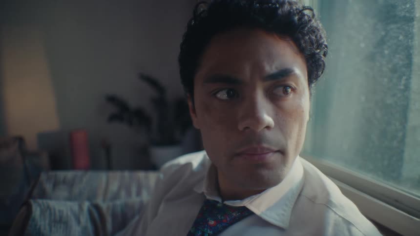 The face of a young man sitting down and he is wearing a white shirt and a tie and looking straight ahead and then looks to his left