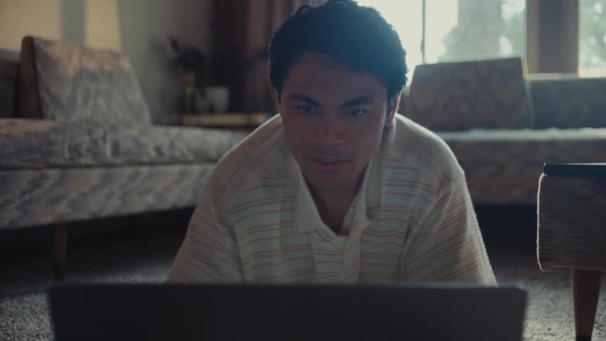 A hispanic man sits on his living room floor while working on his laptop