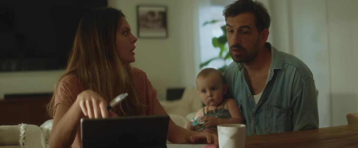 Two adults and a child are seated at a dining table with a laptop open in front