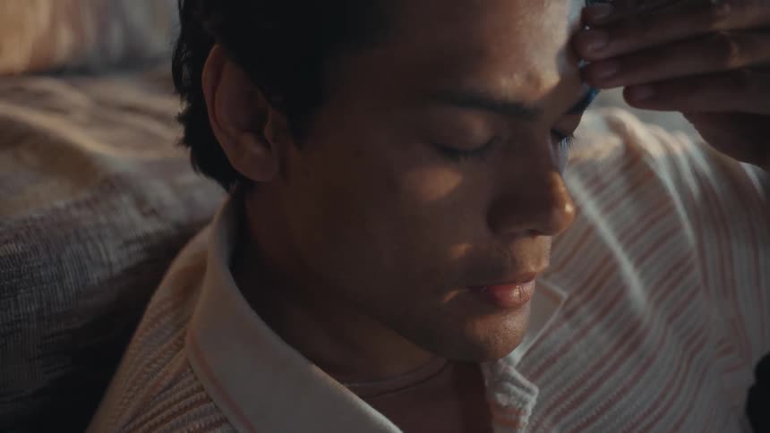 A hispanic man sits on the floor next to his couch while thinking and worrying
