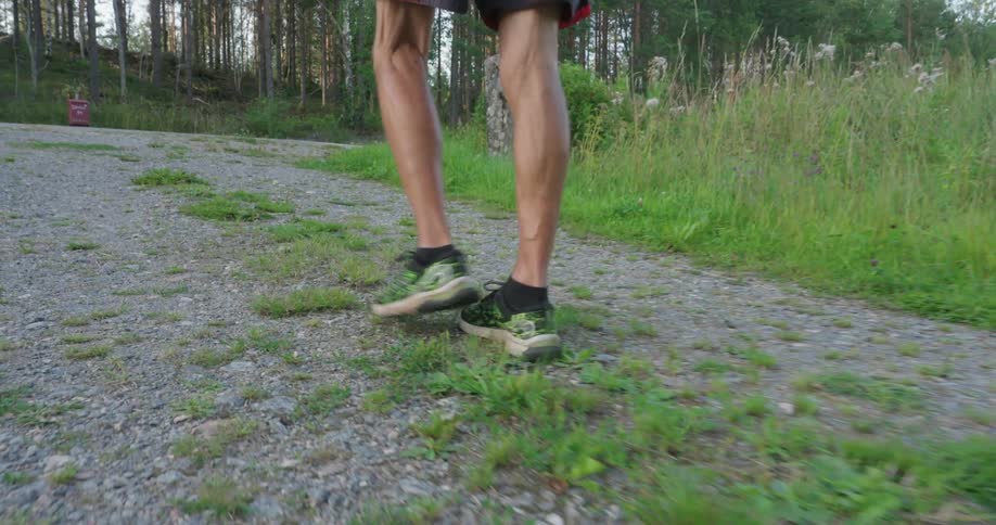 A mans feet and legs in sneakers walking on a gravel walkway