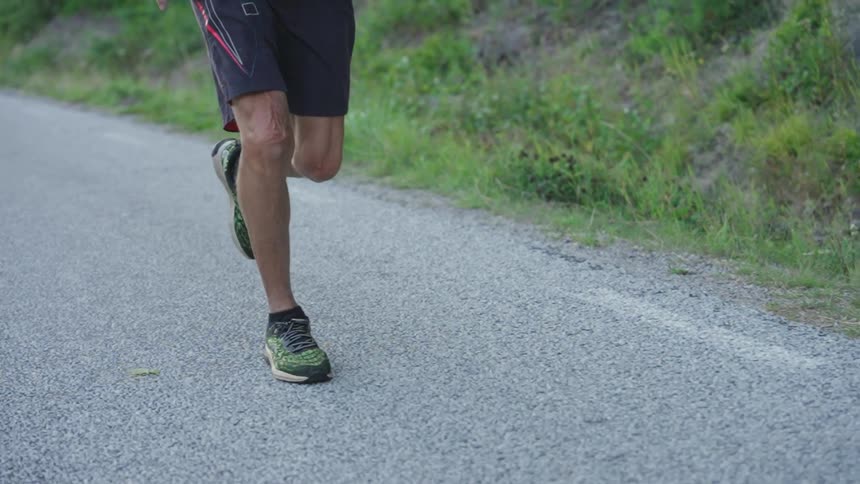 A runners legs and feet in running in slow motion on a paved road
