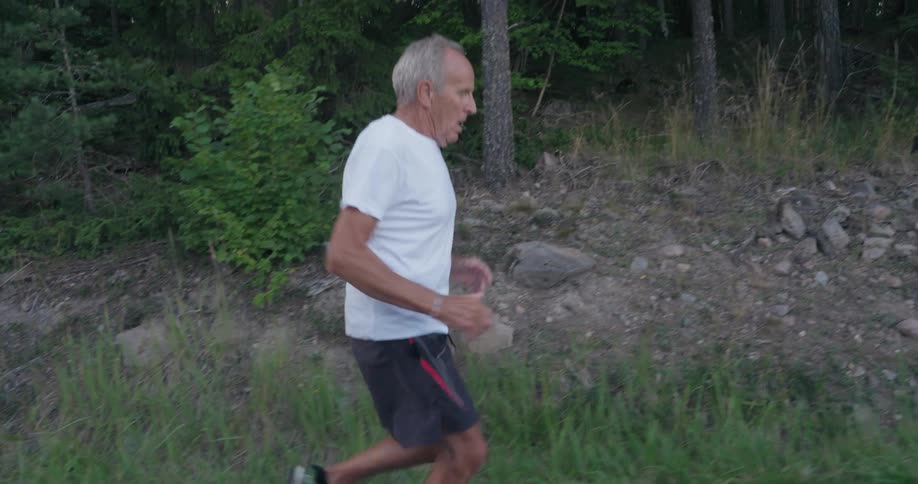 An older man running down a roadway near trees and rocks on the side