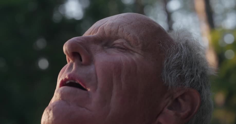 A senior man with a weathered face and gray hair looking up with his eyes closed and mouth slightly open