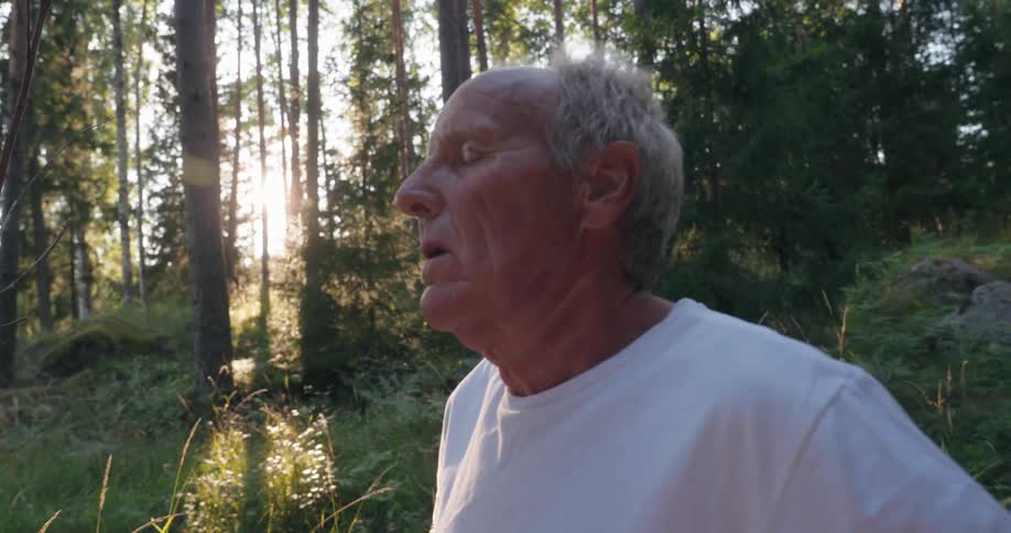 Close up of an older mans face while he stands outside in the trees breathing slowly with his eyes closed