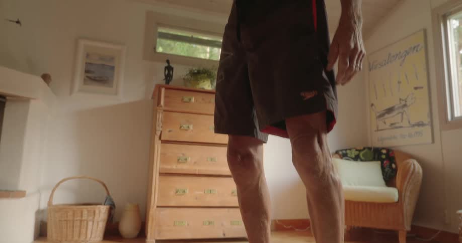 An elderly man does barefoot exercises in his living room