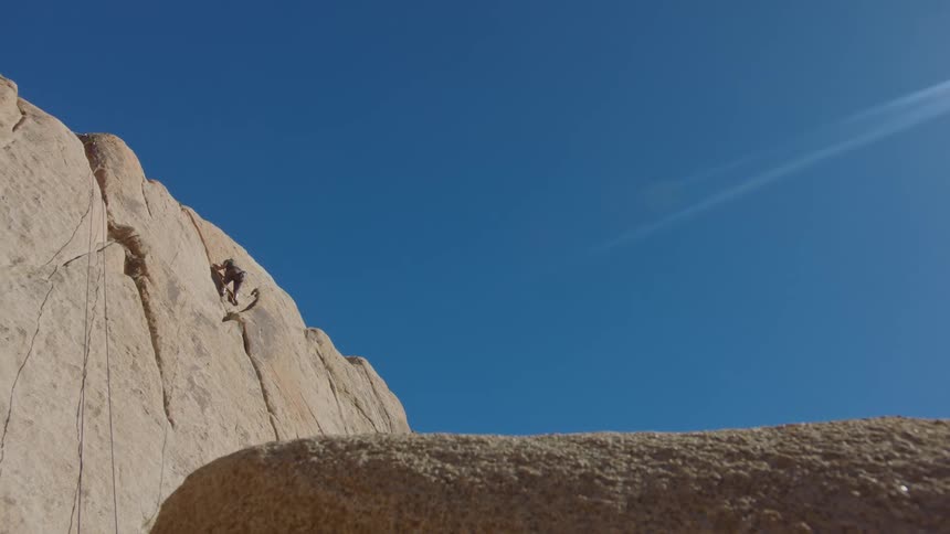 Person climbing a rock wall on a blue sky day