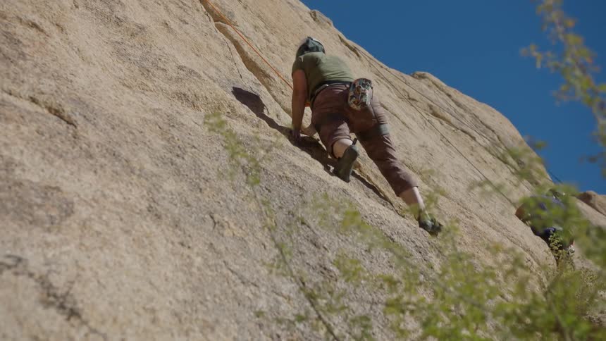 A person is climbing a rock holding onto an orange rope