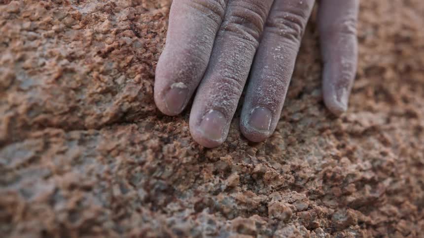 A dirty dusty hand touches a crumbling brown rock