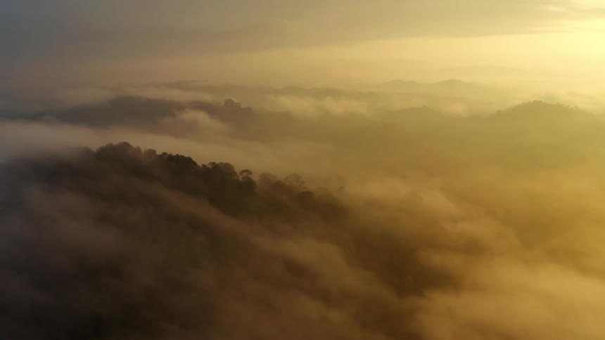 Aerial above the clouds hovering over mountain tops as the sun rises