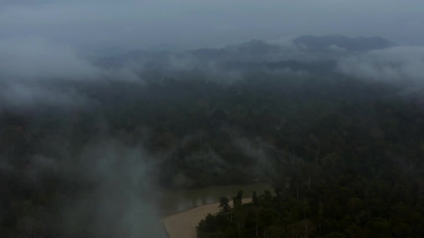 Aerial view of mountains with forests and a lake in the background on a cloudy day