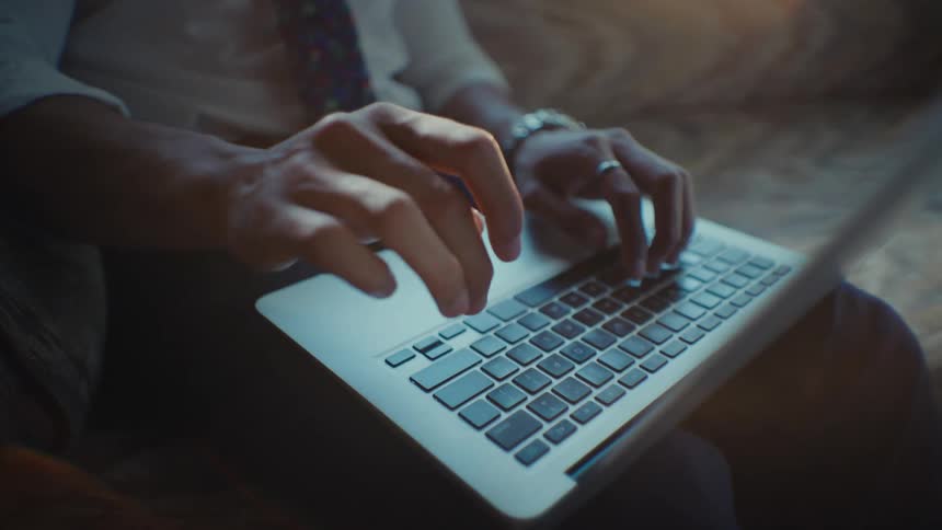 Close up of the hands of a person sitting on a couch while typing on a laptop