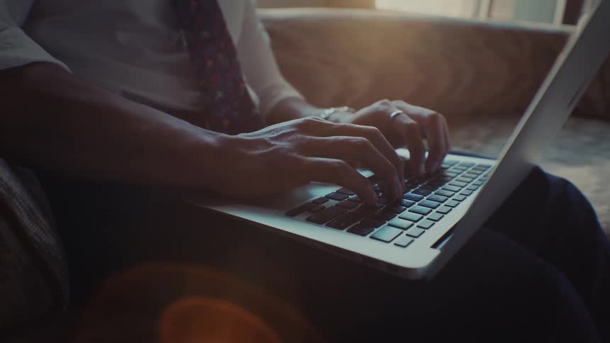 Close up of the hands of a person sitting on a couch while typing on a laptop