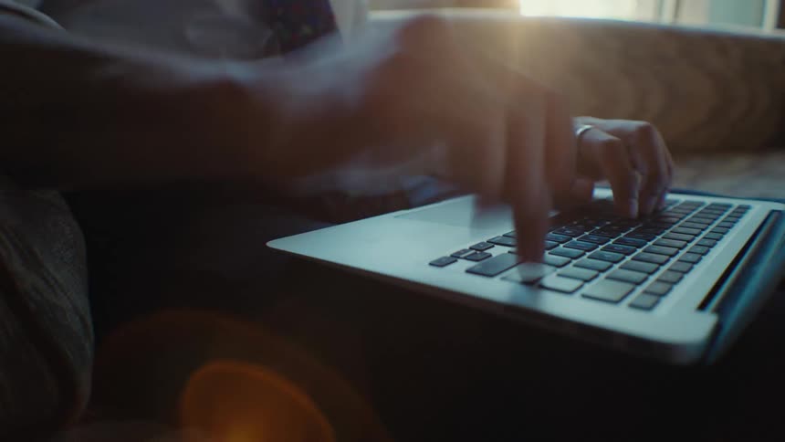 Closeup of a persons hands typing on a laptop while sitting on a couch