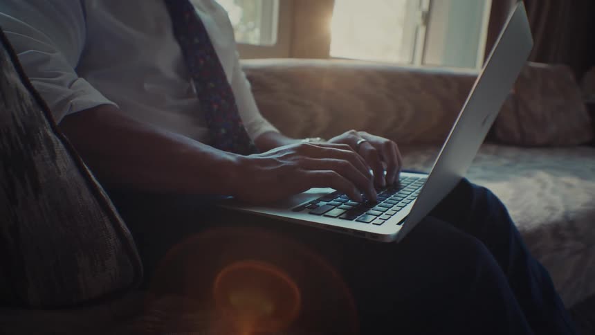 A man sitting on a couch typing on a keyboard on his laptop