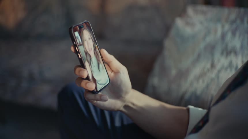A man is holding a smartphone that is displaying a video call with a woman