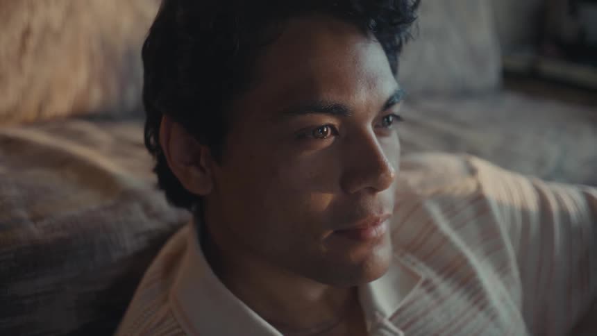 A pensive man sitting on the floor with his back leaning against a couch starts smiling