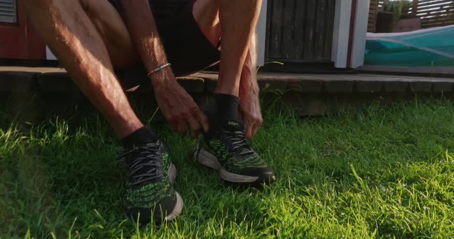 A man sits on the porch tying his shoelaces over green grass