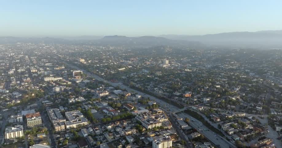 An aerial of a baseball field next to a highway with traffic on it traveling through an urban area