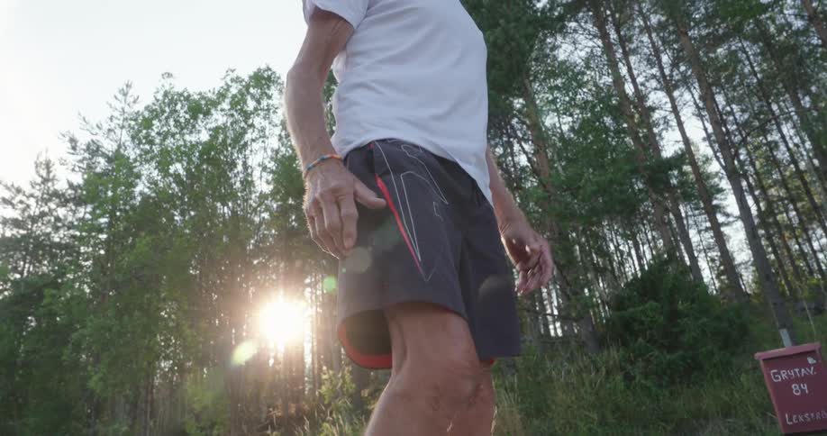 An elderly man in tshirt and shorts stands on a park road warming up before starting a run