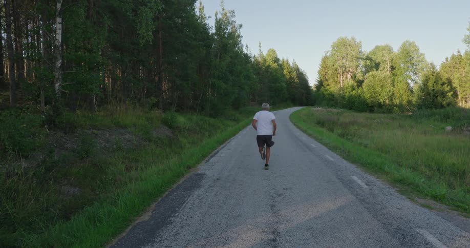 Elderly man running down a narrow road surrounded by vegetation