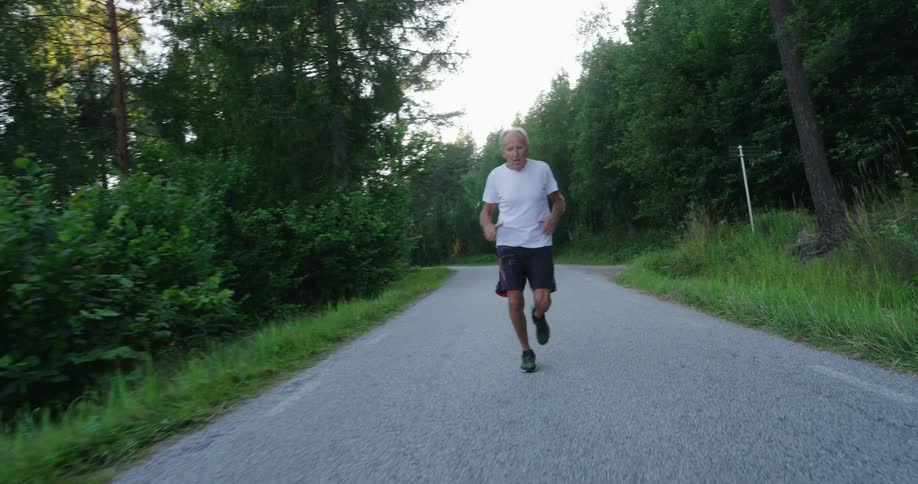 Elderly man running on a paved road surrounded by trees