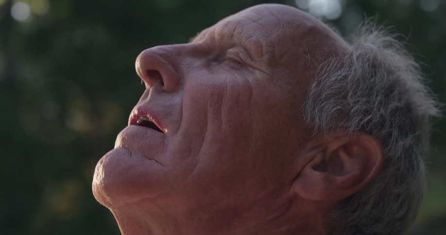 Balding man stands outdoors with his face lifted towards the sky