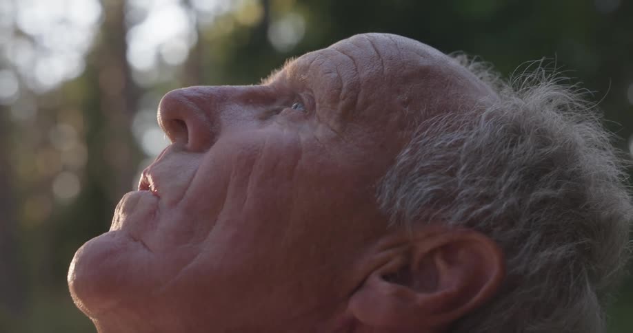 Close up of an older man outside looking up at the sky blinking slowly in relaxation