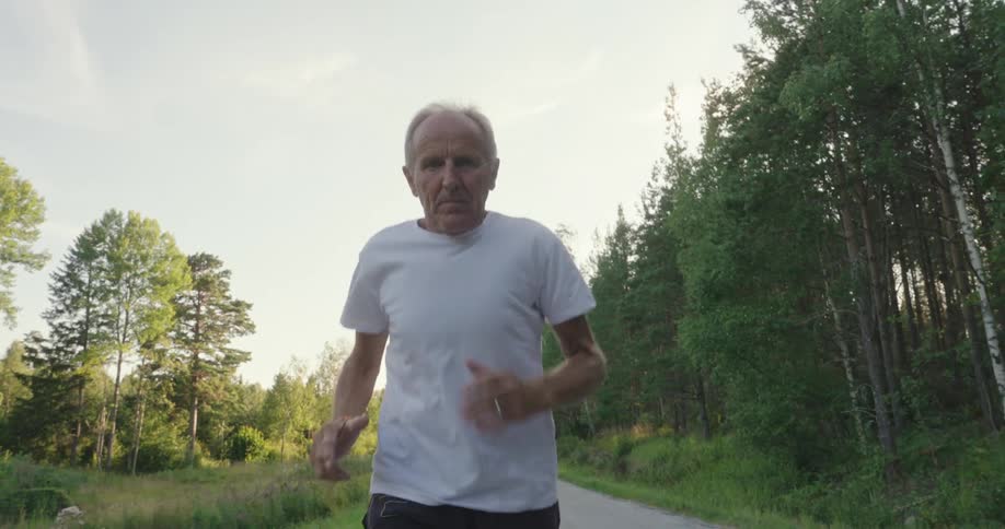 An elderly man jogging on a road near to the forest at morning