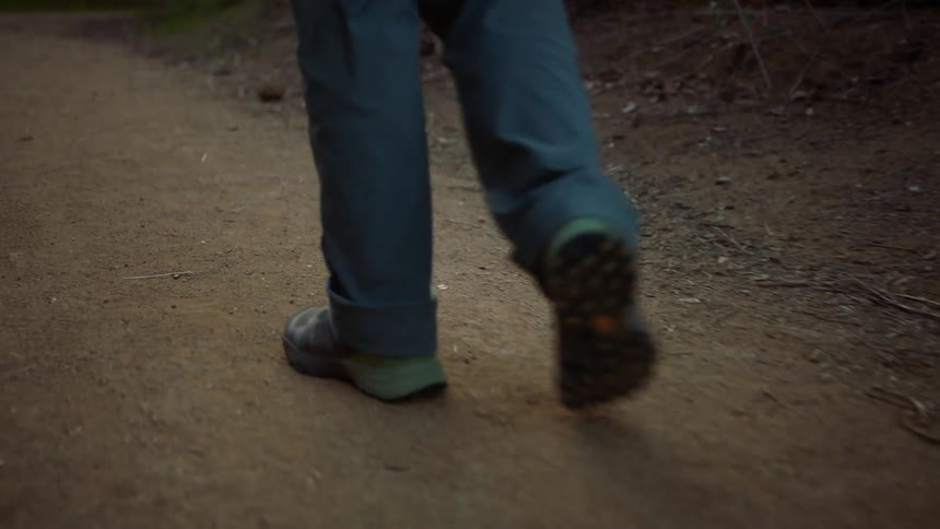 A person wearing jeans walks uphill on an outdoor hiking path