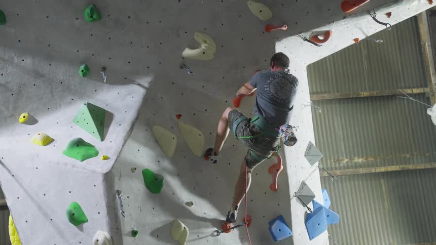 A man climbing a fake rock wall attached to ropes while grabbing at different blocks on the wall