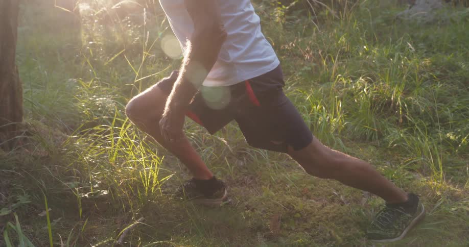 An elderly man stretches his calves while standing against a tree in a forest