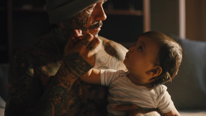 Tattooed father in tshirt sitting playing with his daughter on his lap