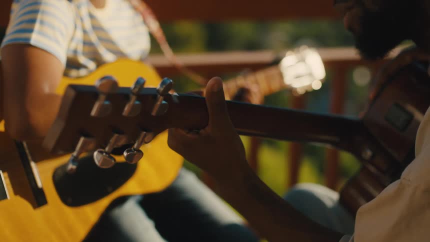 A father teaches his son to play guitar outdoors on a sunny day