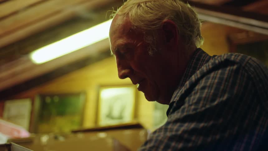 An older man lifting a box up with his arms smiling determined
