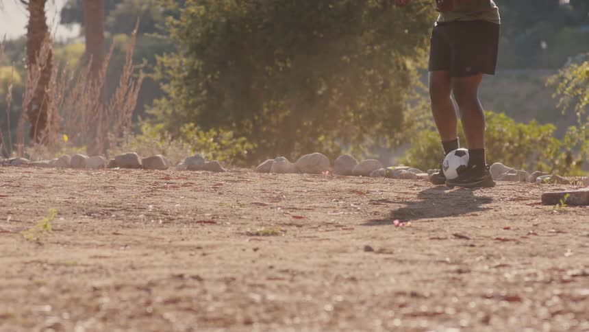 Two friends are playing soccer on a dirt surface kicking small clouds of dust