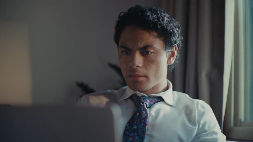 A man in formal attire sits on the living room working on a laptop