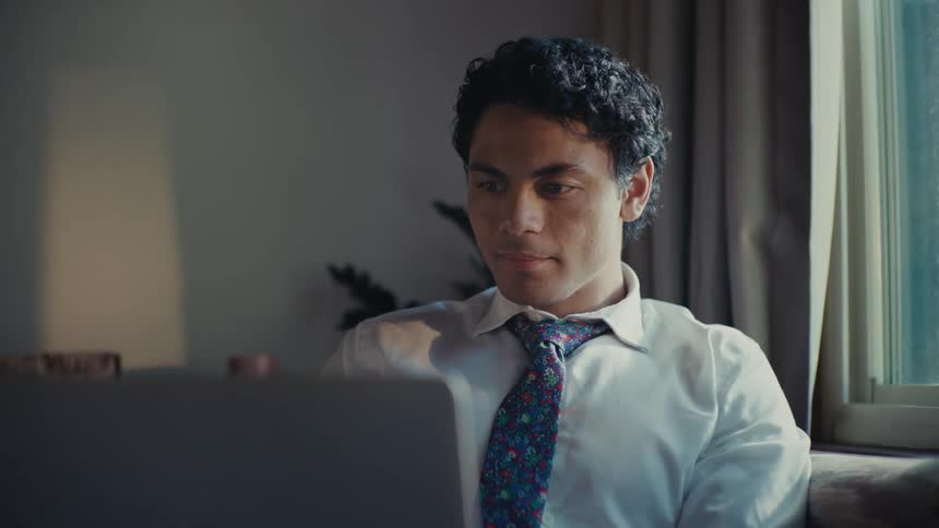A hispanic man works on his laptop while sitting on a couch
